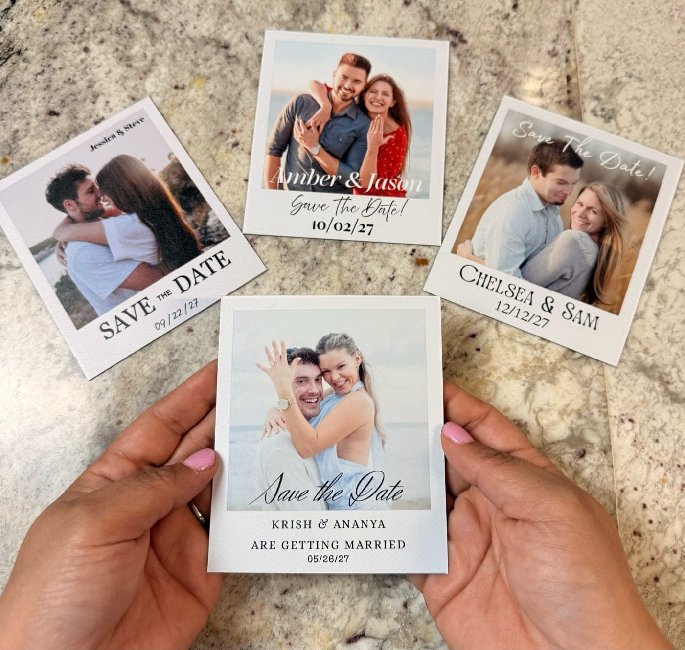 Four flexible save-the-date photo magnets held in two hands over a marble countertop, each a different engaged couple.